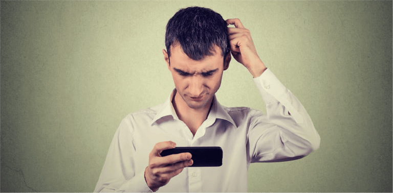 Closeup portrait perplexed young man looking at smart phone seeing bad news or photos with confused emotion on his face isolated on gray wall background. Human reaction,