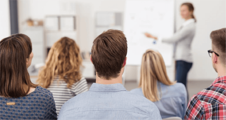 Rear View of Young Office Workers in Casual Outfits Listening to a Top Manager Explaining Something Using Illustrations.