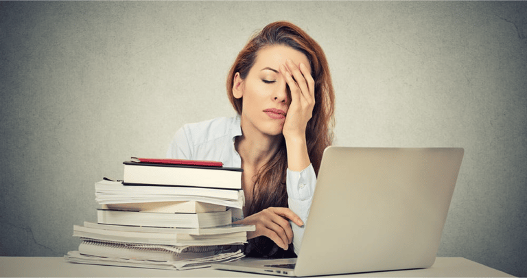 Too much work tired sleepy young woman sitting at her desk with books in front of laptop computer isolated grey wall office background. Busy schedule in college, workplace, sleep deprivation conc