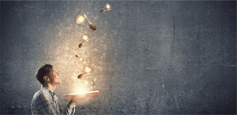 Young man holding opened book with glass glowing light bulbs flying out
