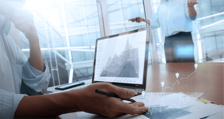 business documents on office table with smart phone and laptop computer and graph business with social network diagram and two colleagues discussing data in the backgro